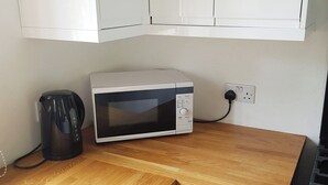 A kitchen with a white microwave, a black coffee maker, and a wooden countertop. - 1 bedroom accommodation in Rosemarkie (Rosemarkie)