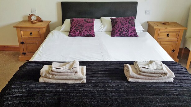 A neatly made bed with two pillows, a wooden nightstand with a clock, and a bedside table with a lamp. - 1 bedroom accommodation in Rosemarkie (Rosemarkie)