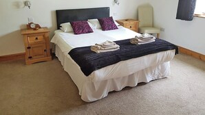 A neatly made bed with white linens and two purple pillows, a wooden nightstand with a clock, and a chair against the wall. - 1 bedroom accommodation in Rosemarkie (Rosemarkie)