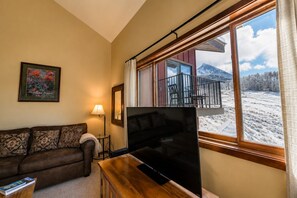 A living room with a sofa, a TV, a lamp, and a window with a view of a snowy landscape.