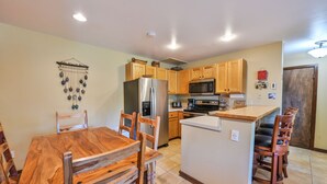 A kitchen with wooden cabinets, a stainless steel refrigerator, a microwave, and a wooden dining table with chairs. - Ski-In/Ski-Out, Hot Tub, Fireplace & Mountain Views (Crested Butte)