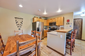 A kitchen with wooden cabinets, a stainless steel refrigerator, a microwave, and a wooden dining table with chairs. - Ski-In/Ski-Out, Hot Tub, Fireplace & Mountain Views (Crested Butte)