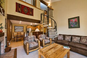 A spacious living area with a wooden coffee table, two patterned armchairs, a brown sofa, and a spiral staircase leading to an upper level.