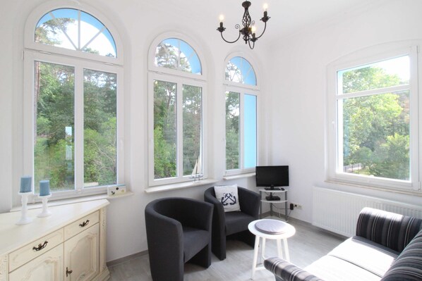A room with a white cabinet, two armchairs, a sofa, a TV, and a chandelier.