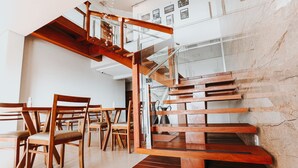 Un interior modern amb una escala de fusta, baranes de vidre i una zona de menjador amb cadires i taules de fusta.