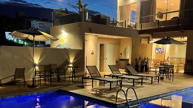 Una piscina amb gandules i ombrel·les, un restaurant i un edifici amb balcó.