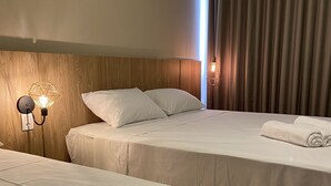 Habitació d'hotel amb dos llits, un capçal de fusta, una petita taula de nit amb una làmpada i una finestra amb cortines.