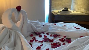 Un llit ben fet amb una tovallola modelada com un cigne i una rosa, envoltat de pètals de rosa dispersos.