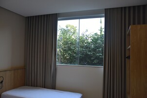 Habitación de hotel con una cama individual, ventana con cortinas y vista a zonas verdes.
