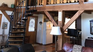 Ein rustikales Blockhaus-Interieur mit einer Holztreppe, einem Schlafbereich mit Holzwirbeln, einem Ledersofa und einem Essbereich.