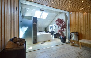 Ein moderner Wellnessbereich mit Glaswand, Holzvertäfelung, einer großen Badewanne und einem Blumentopf.