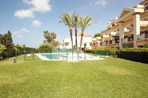 A pool surrounded by a well-maintained lawn, palm trees, and a multi-story building with balconies.