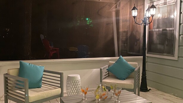 Een overdekt buitengebied met twee houten stoelen, een tafel met drankjes en een lantaarnpaal.