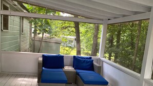 Een overdekt terras met rieten meubels en blauwe kussens, met uitzicht op een groen landschap.