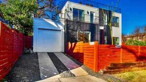 Una casa moderna de dos pisos con puerta de garaje blanca, cerca roja y cielo azul despejado.