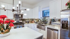 Una cocina moderna con armarios blancos, electrodomésticos de acero inoxidable, encimera de mármol y una lámpara decorativa.