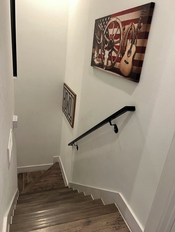 A staircase with wooden steps, a handrail, a wall-mounted picture of a guitar and an American flag, and a framed geometric design.