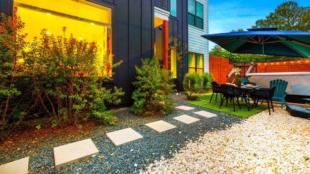 Una casa moderna con un patio que cuenta con una barbacoa, asientos al aire libre y un jardín bien cuidado.