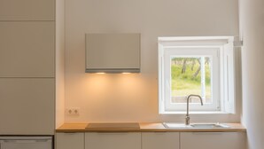 Een moderne keuken met witte kastjes, een inbouwoven en een raam met uitzicht op groen.