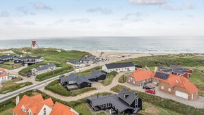 Zona residencial costera con casas, una playa y una estructura roja a lo lejos.