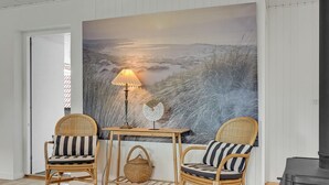 Una habitación acogedora con dos sillones de mimbre, una mesita y una lámpara. En la pared, un cuadro grande de un paisaje nevado.