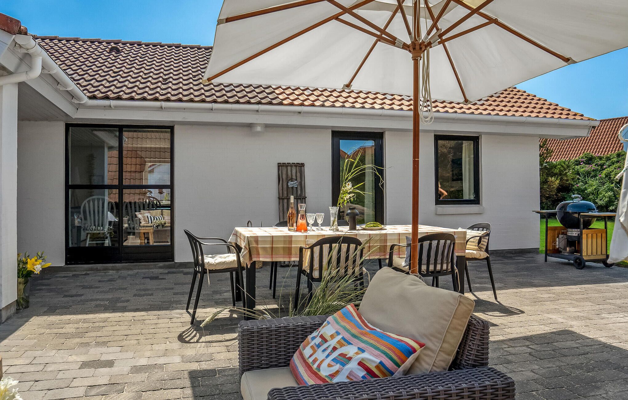 Eine Terrasse im Freien mit einem Esstisch, umgeben von Korbstühlen und einem großen Sonnenschirm.