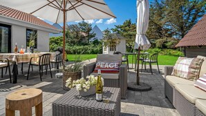 Un patio exterior con mobiliario de mimbre, una mesa dispuesta con una botella de vino y una almohada con la palabra 'PEACE'.