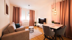 A modern living room with a sofa, dining table, chairs, a TV, and a small side table. - Cherry Apartment for Families and Couples with Free Parking (Zadar)