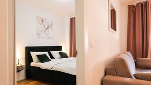 A bedroom with a bed, a nightstand, a wall-mounted mirror, and a window with curtains. - Cherry Apartment for Families and Couples with Free Parking (Zadar)