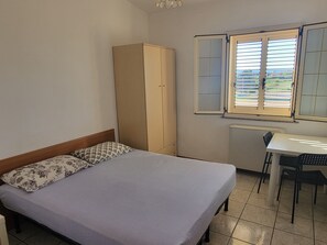 Une chambre à coucher avec un lit, une armoire, un bureau et une fenêtre avec des stores.
