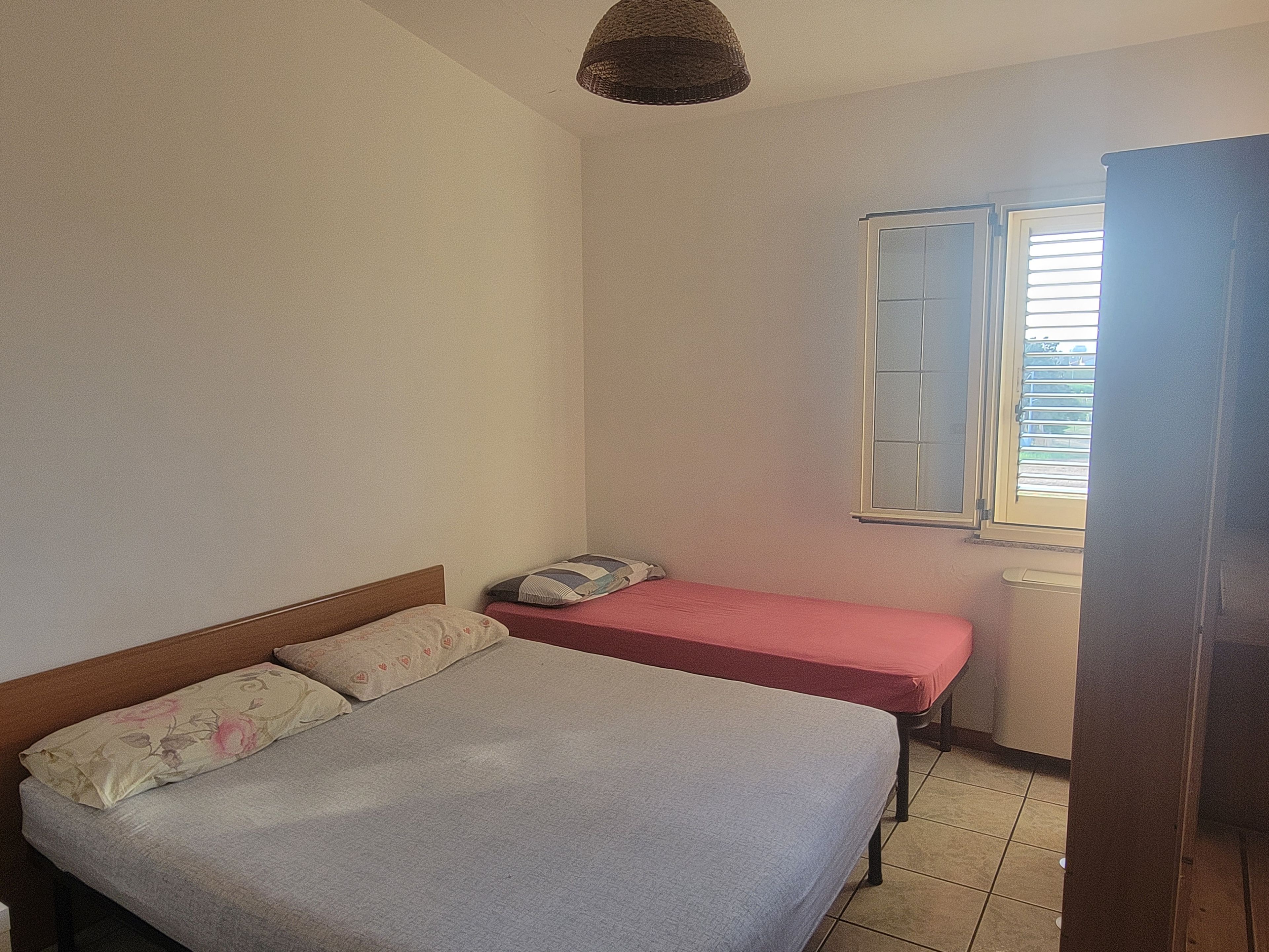 Un dormitorio con dos camas, una ventana con persianas y una lámpara colgante.