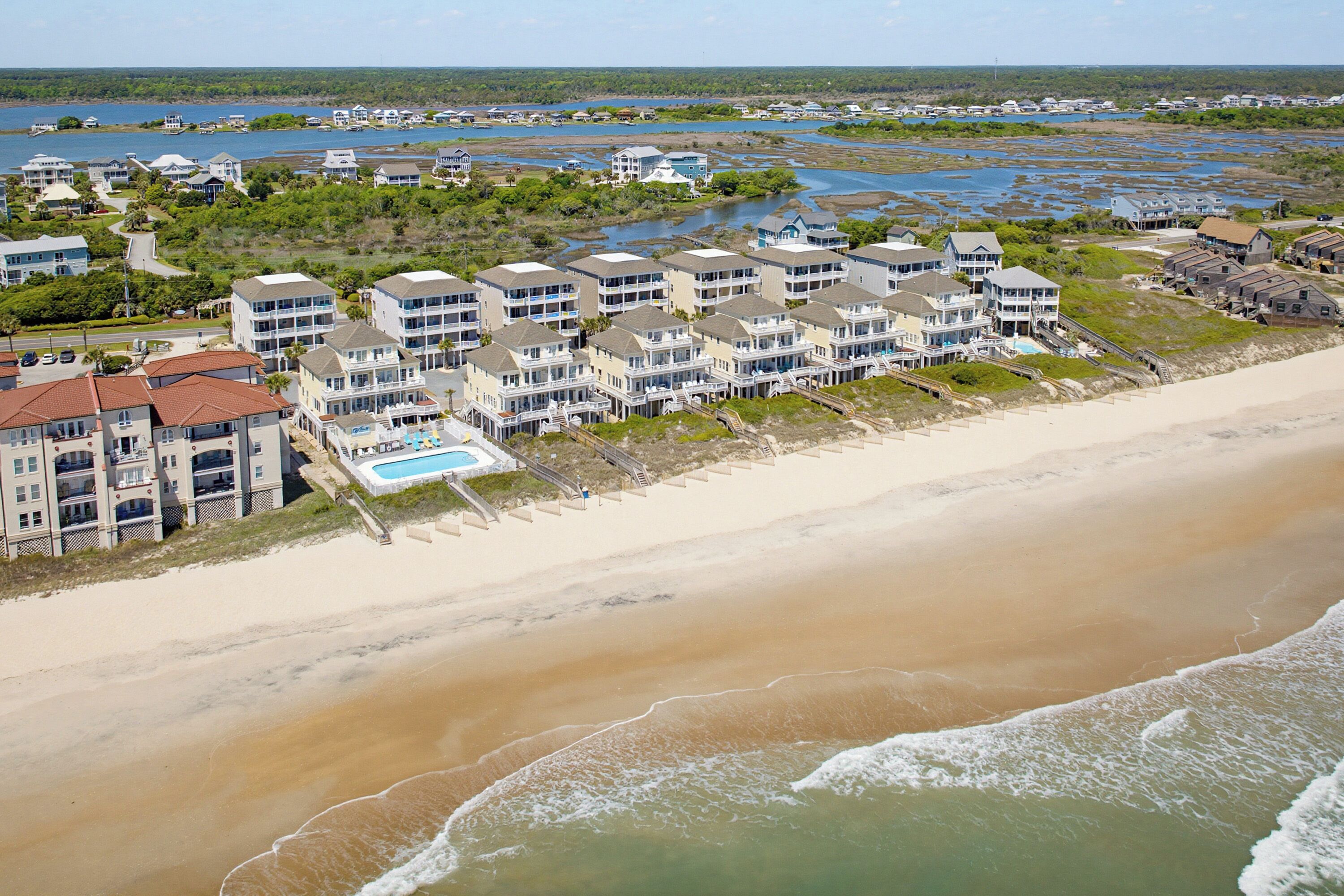 A beachfront hotel with multiple-story buildings, a swimming pool, and a beach area.