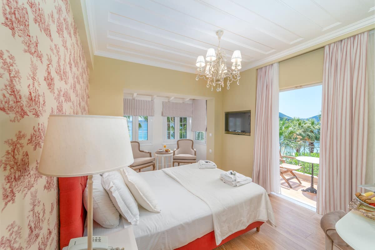 Habitación de hotel con cama, escritorio, silla, televisor y balcón con vista a las montañas.