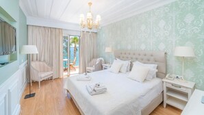 A hotel room with a large bed, two bedside tables, a chandelier, and a view of the outdoors. - Hotel Orion (Lefkada)