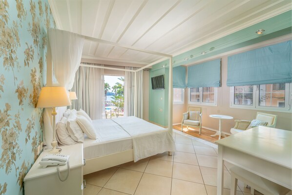 Quarto de hotel com cama, escrivaninha, cadeira, telefone e janela com vista para palmeiras.