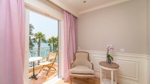 A balcony with a chair and table, a view of palm trees, and a door with pink curtains. - Hotel Orion (Lefkada)