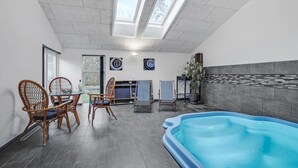 Ett modernt inomhusbadområde med ett glastak, ett matbord med stolar och en sittgrupp med en krukväxt.