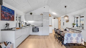 Ett modernt kök med vita skåp, en köksö och en matplats med bord och stolar.
