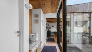 Un interno moderno con soffitto in legno, un'accogliente zona salotto con una coperta in pelliccia e vista sullo spazio esterno adiacente.