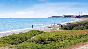Una spiaggia con persone, una barca e una nave all'orizzonte.