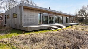 Una casa moderna con tetto piatto, ampie finestre e un terrazza in legno.