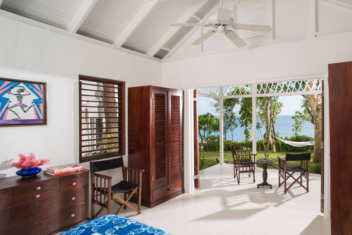 Une chambre spacieuse avec un grand lit, un bureau avec une chaise et une vue sur l’océan grâce à une porte-fenêtre coulissante.