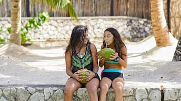 Two individuals sitting on a stone bench outdoors, holding coconuts.