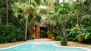 Una piscina rodeada de exuberante vegetación tropical y una estructura con techo de paja.