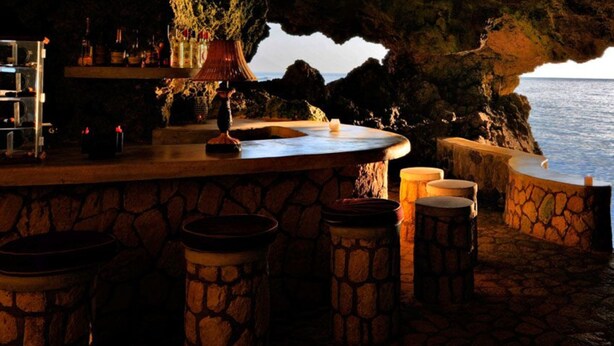 Un bar con taburetes de piedra y vistas al mar a través de una estructura que se asemeja a una cueva.