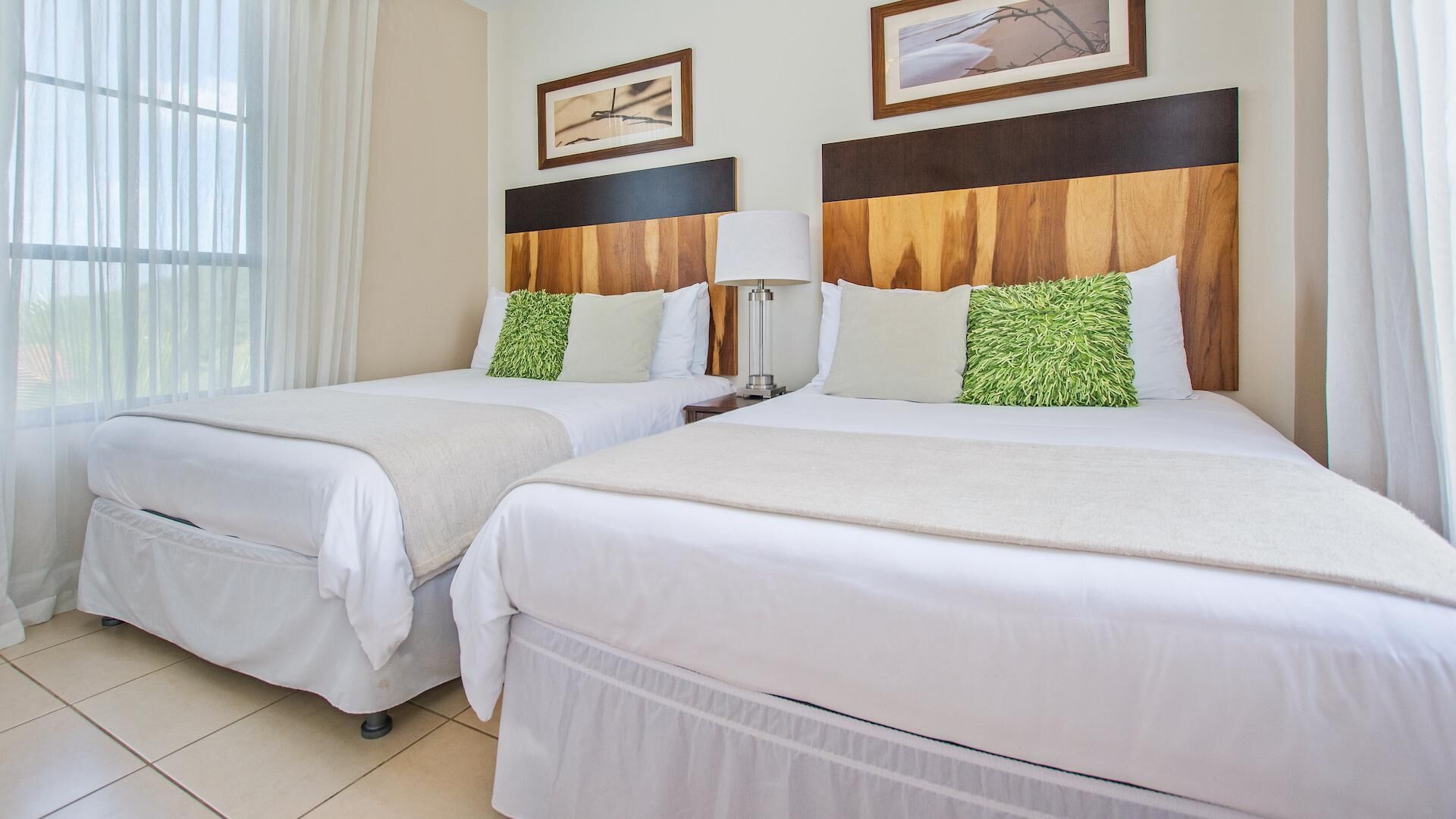 Habitación de hotel con dos camas, una mesita de noche, una lámpara y dos cuadros en la pared.