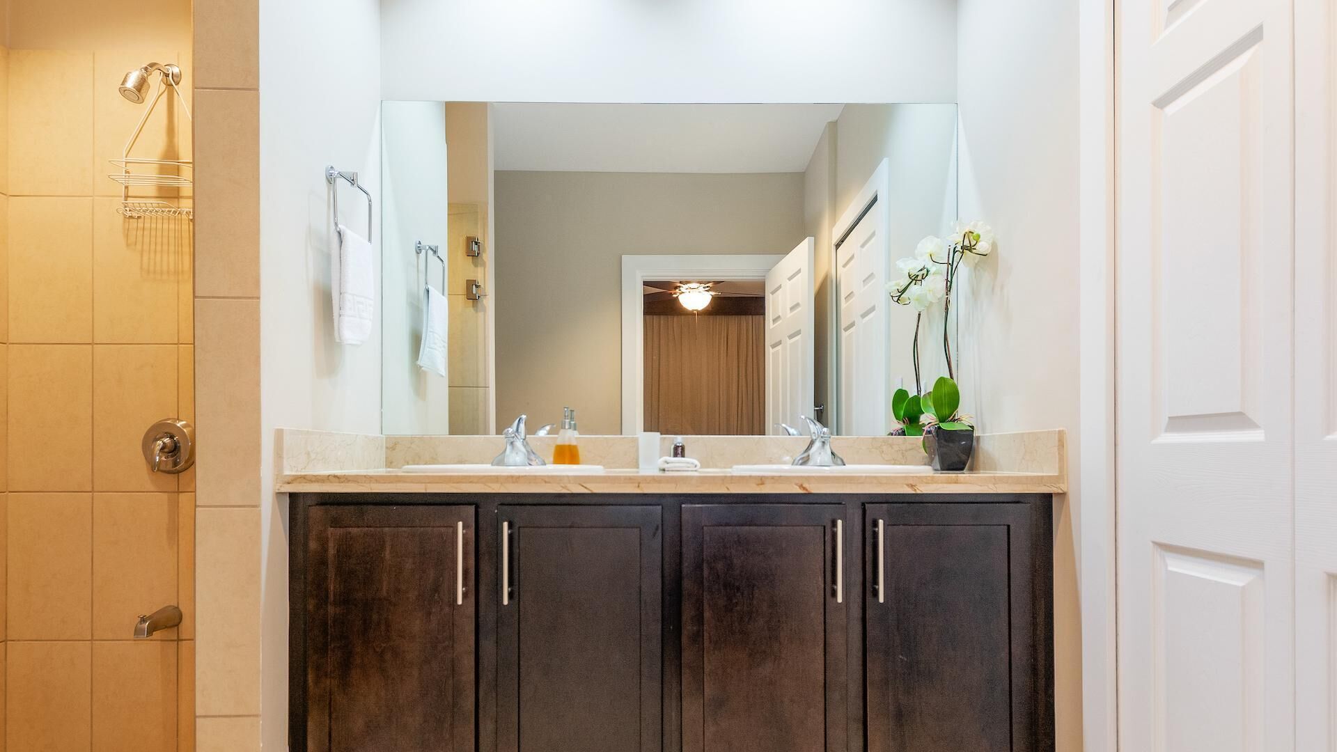 A bathroom with two sinks, a large mirror, dark wooden cabinets, and a shower area.