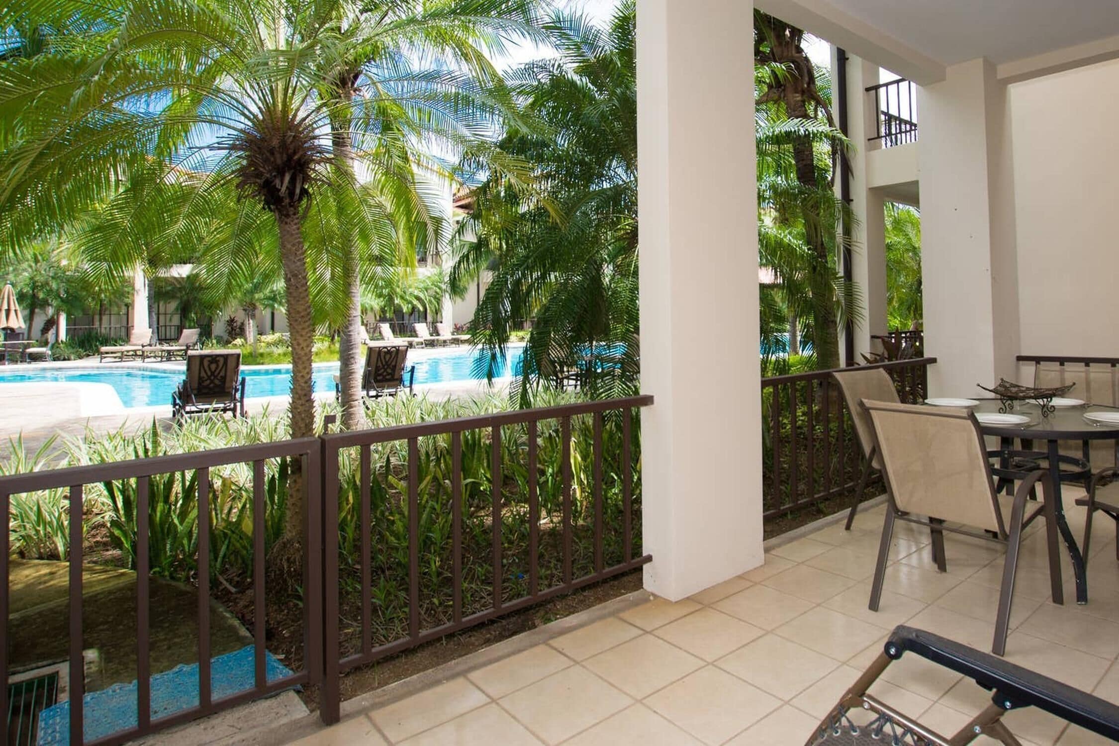 Un balcon avec une piscine, des palmiers et un coin repas comprenant des chaises et une table.