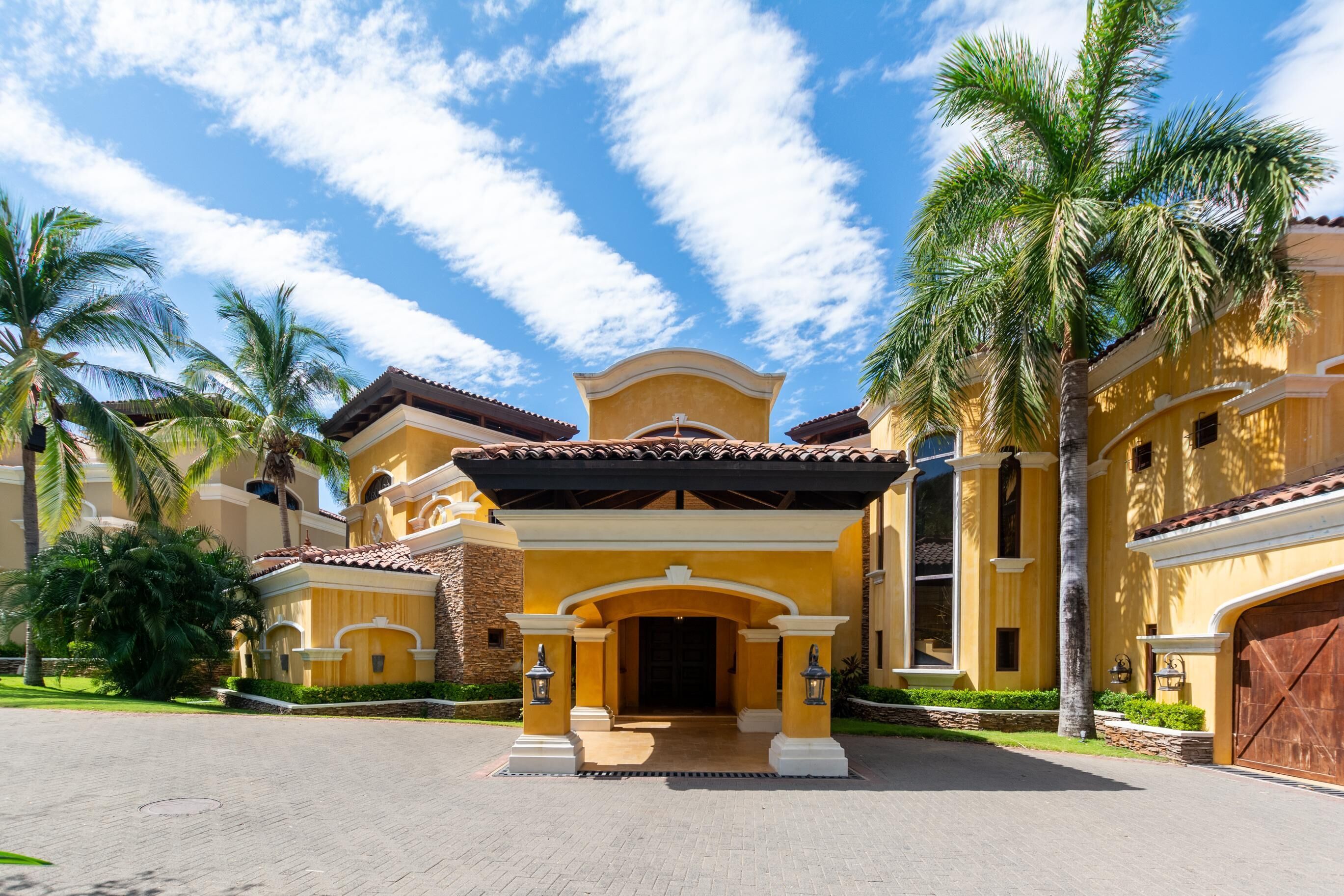 A yellow building with a central entrance, palm trees, and a clear blue sky.