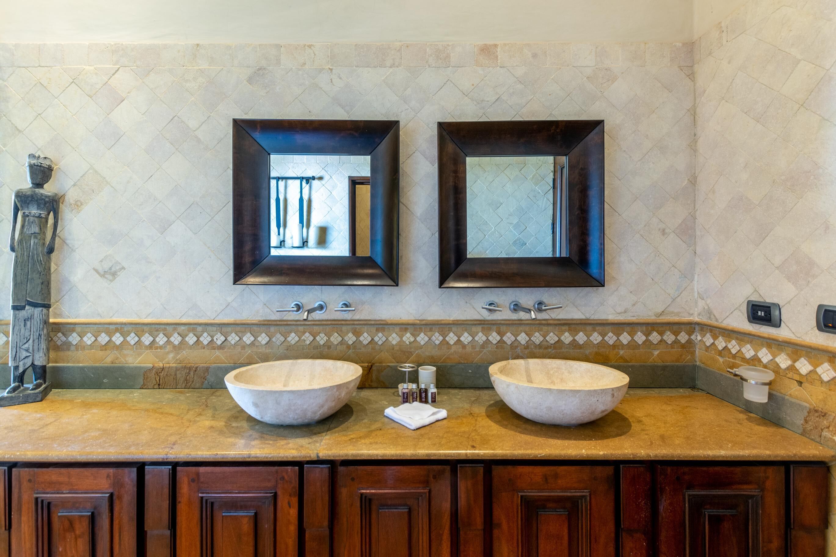 A bathroom with two large stone sinks, wooden cabinets below, and a decorative statue on the left.